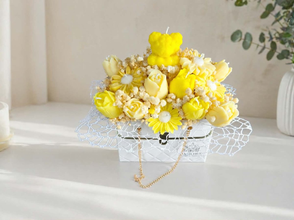 Bright yellow and cream flowers in a white patterned box with mesh ribbon on a white shelf