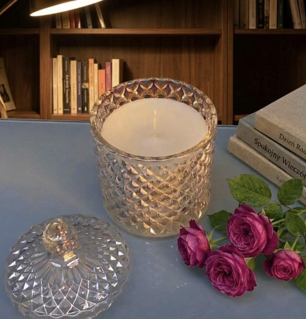 Decorative crystal candle with textured glass exterior, matching lid, and magenta roses beside it on a blue surface